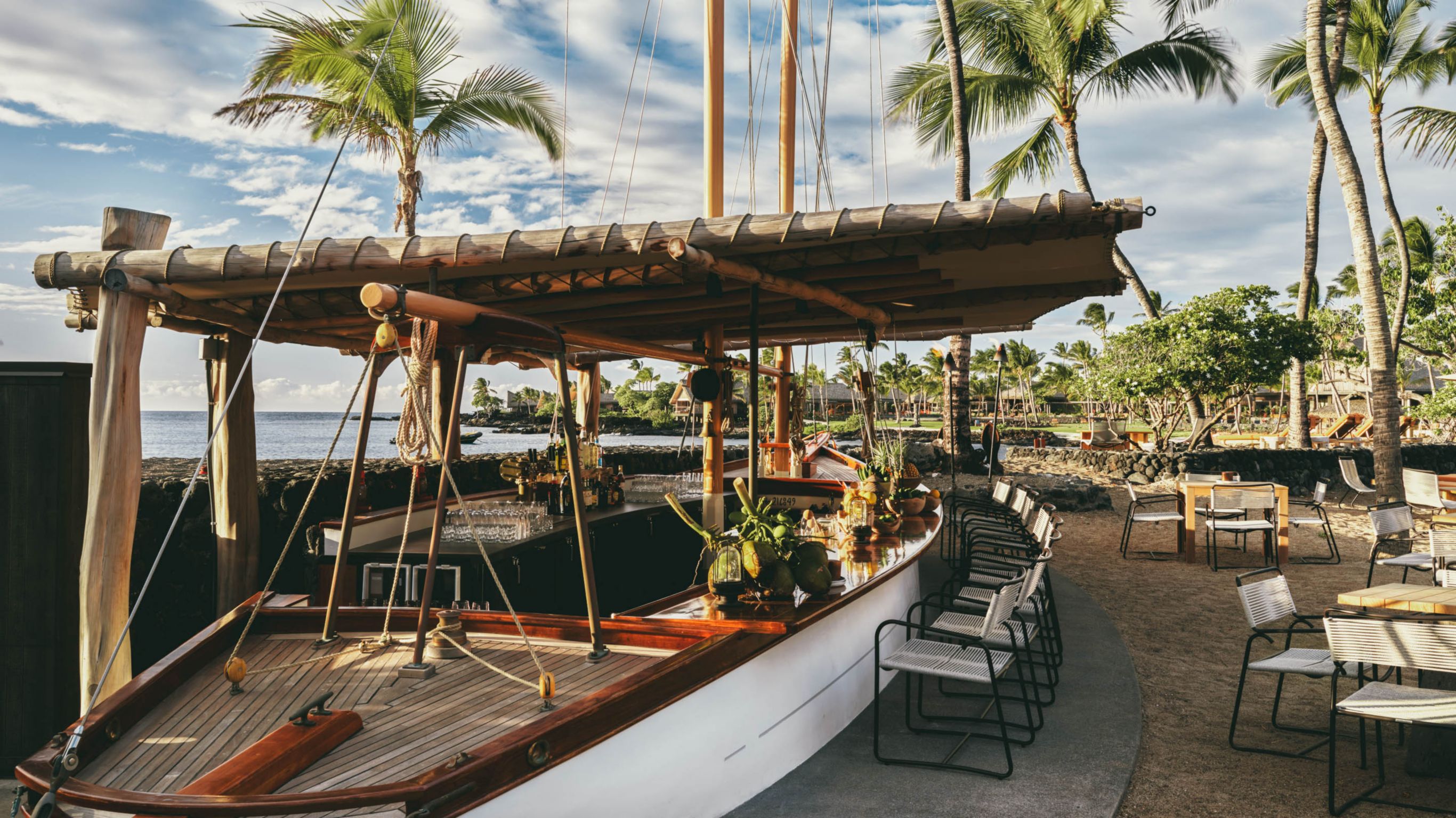 A repurposed boat serves as a beachside bar  featuring chairs and ocean views.